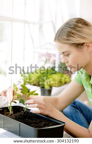 Beautiful young woman working in greenhouse. Woman planting two green sprouts