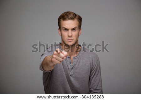 Portrait of handsome stylish young man on grey background. Serious and self-confident man looking and pointing at camera