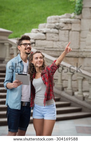 Portrait of beautiful young woman and handsome man on vacation. Smiling girl pointing at something on excursion. Boy holding tablet computer