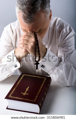 Photo of sad old man praying to God with rosary and Bible