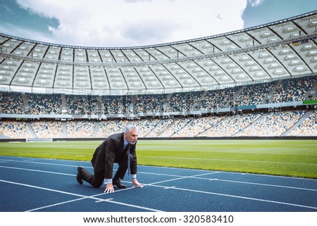Side view photo of confident aged businessman lined up getting ready for race on modern sport track. Stadium as a background