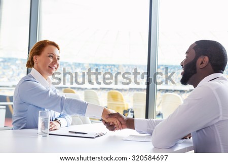 Photo of creative multi ethnic business people. Mixed race business people smiling and shaking hands while meeting. White modern office interior with big window
