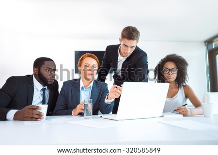Photo of creative multi ethnic business group. Mixed race business team using laptop and discussing project. White modern office interior