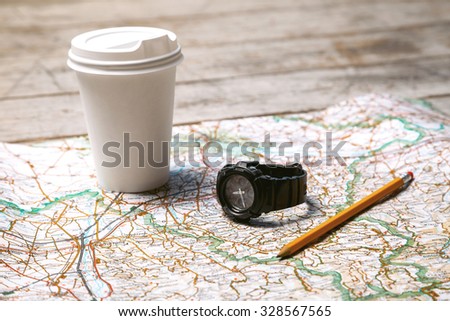 Photo of world map, white cup of coffee, pencil and watch. Objects are on light colored wooden floor