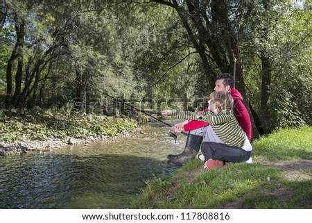 Father and son sitting by the river and learning how to fish