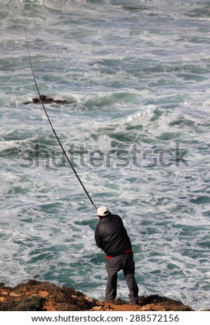 SAGRES, PORTUGAL - SEPTEMBER 29 : An unknown sea angler, fishes for sea bream from a precarious position on a rock, overlooking a wild Atlantic Ocean - on September 29, 2010. Sagres, Portugal.