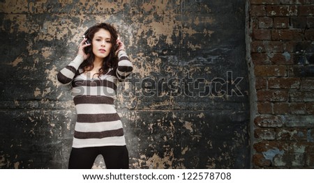 Young woman listening to music through headphones beside a grunge wall ideal for club graphics or event text