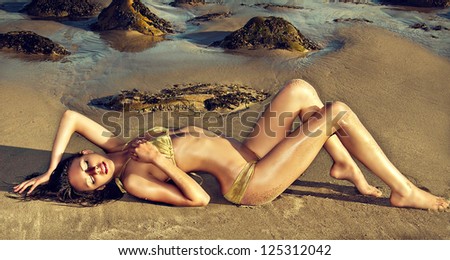 Beautiful exotic young woman lying on rock on beach