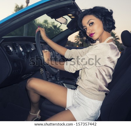 Beautiful young woman stepping out of luxury car