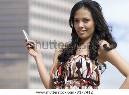 Attractive Asian American woman holding cell phone with corporate skyscraper in the background.