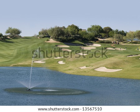 View of golf course from club house green, with lake and water fall in foreground and holes in distance.