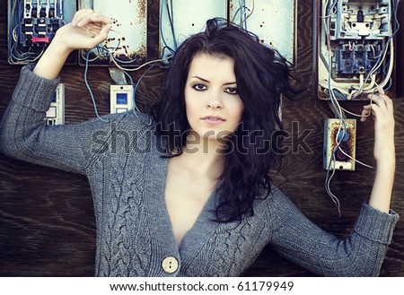 Beautiful young emo goth styled woman with long brunette hair posing against decaying electrical wiring system.