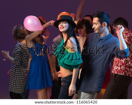 young beuatiful gilr smiling to the camera, dancing with young guy, with people dancing in the background