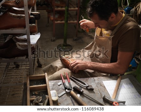 adult man working in a shoe factory, sewing the soles of the shoes manually