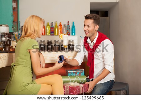 young handsome guy asking his girlfriends hand in marriage in colorful cafe with gift boxes