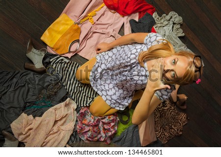 young woman sitting in a pile of clothes looking surprised, covering her mouth with her hand