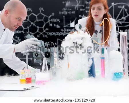 close-up of a teacher in a chemistry lab conducting an experiment around lab tools, colorful liquids and gas with a student observing reactions on the background