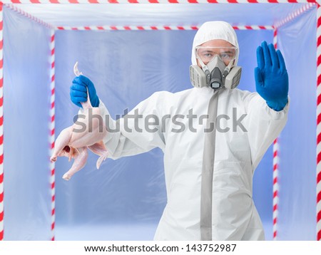 Biohazard technician in a full biohazard suit and breathing apparatus holding up a bird carcass and gesturing to stop warning of an outbreak of the bird flu virus