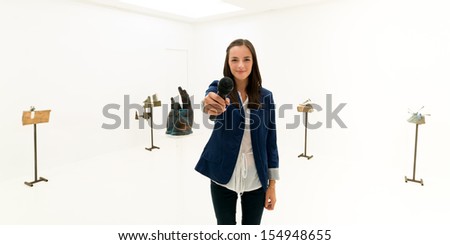 front view of woman standing, smiling and holding a microphone in her hand, taking an interview in an art gallery