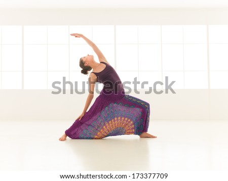 front view of young  woman in balanced yoga pose, dressed colorful indor studio