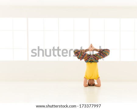 close up of single young man in advanced yoga posture, dressed colorful, in studio gym
