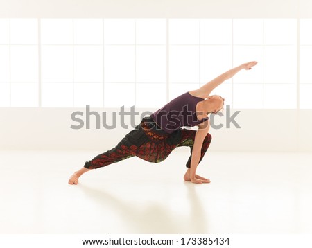 young  woman demonstrating advanced yoga posture, in an empty room with natural light.