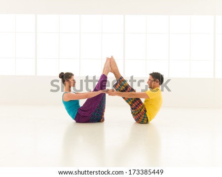 beautiful woman with a handsome man dressed in vibrant colors are partners yoga in white gym