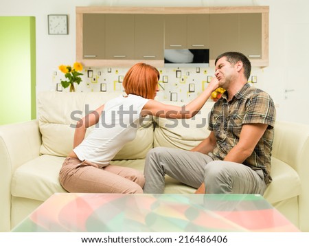 young upset caucasian woman sitting on sofa, punching man sitting next to her