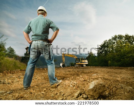 back view of male engineer standing on construction site evaluating the progress