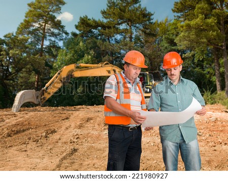 two caucasian engineers on construction site looking at plan and discussing it