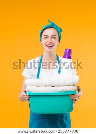 happy cleaning woman holding basin with clean towels and detergent, on yellow background