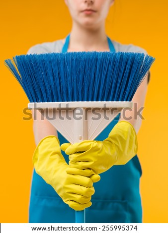 close-up of cleaning woman holding blue broom in front of her, on yellow background