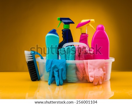 cleaning products and utensils in plastic basin against yellow background