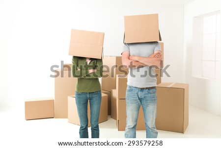 couple with boxes on their heads standing in their new house, arms crossed against their chests