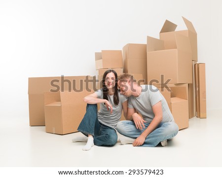 young happy couple sitting on floor in new apartment, exhausted after moving boxes
