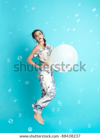 beautiful, happy, young woman jumping with an inflatable balloon in her hand, surrounded by soap balloons.