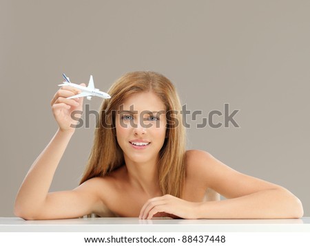 studio portrait of beautiful, young woman, playing with a small airplane model, smiling