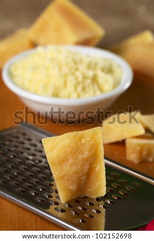 Italian hard cheese on rasp with grated cheese in bowl in the back on wooden board (Selective Focus, Focus on the upper part of the cheese part in the front)