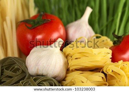 Raw tagliatelle paglia e fieno (straw and hay) with raw garlic bulb and globe tomato (Selective Focus, Focus on the front of the upper yellow tagliatelle pile and parts of the garlic bulb beside)