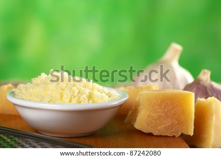 Grated Italian hard cheese with a piece of cheese beside (Selective Focus, Focus on the top of the grated cheese pile and the front upper edge of the cheese piece beside)