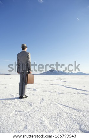 Traveling businessman standing ready with briefcase looking out on dramatic desert horizon