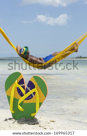 Brazilian man relaxing in hammock over the sea leaving his Brazil flag flip flops in the sand