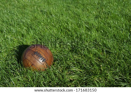 Vintage old brown football old-fashioned soccer ball sits in sunny green grass field
