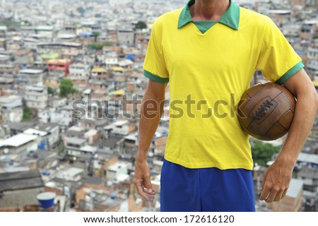 Brazilian football player standing in Brazil team colors holding vintage soccer ball in front of favela slum background in Rio de Janeiro