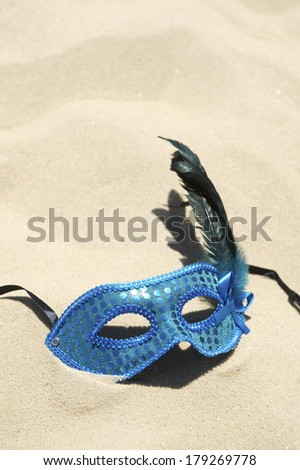 Glittery blue carnival mask with feathers on bright sand Brazilian beach