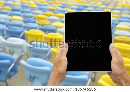 Hands holding blank tablet computer in front of colorful stadium seats
