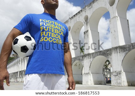 Brazilian soccer player wearing international football shirt holding soccer ball at Arcos da Lapa Arches in Rio de Janeiro