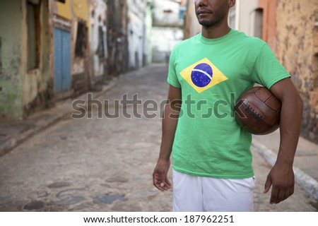 Brazilian football player stands holding vintage brown soccer ball on an old rustic village street