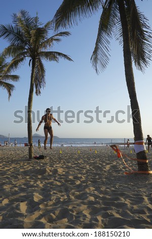 Rio de Janeiro, Brazil - January 27, 2014: Man balances on slackline strung between palm trees on Ipanema Beach.