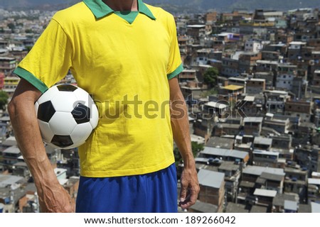 Brazilian football player standing in Brazil colors holding soccer ball in front of favela slum background in Rio de Janeiro